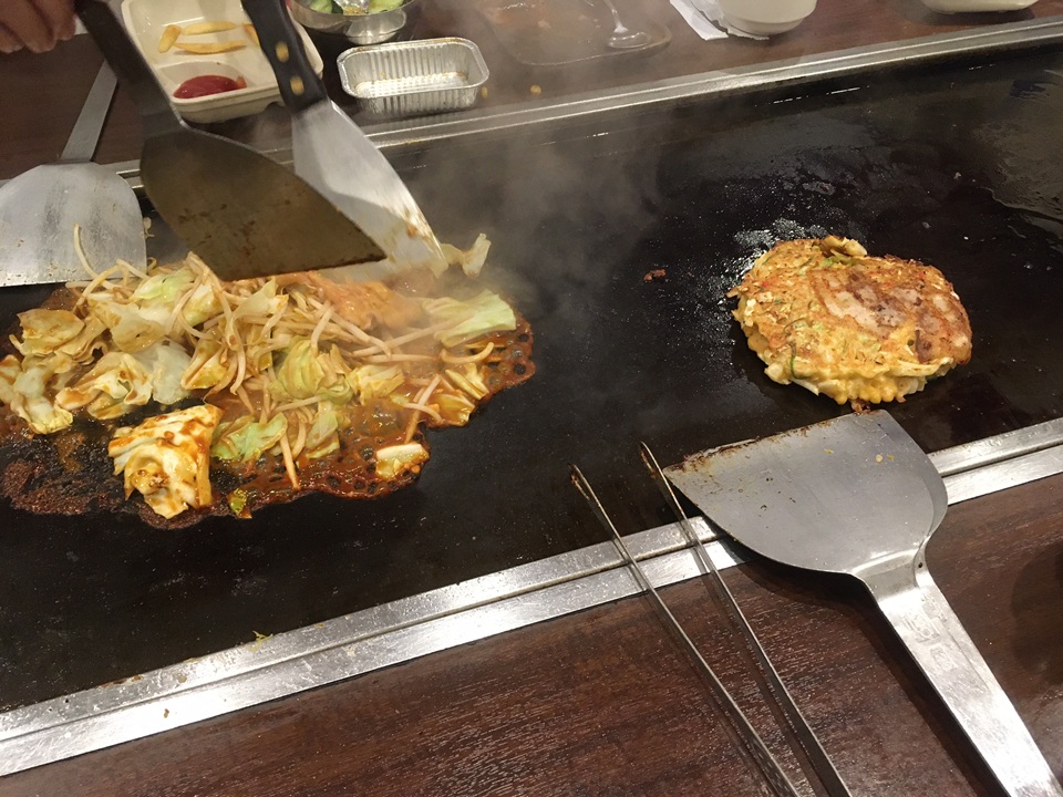 ヘラを使って熱々のお好み焼きと焼きそばを調理している様子